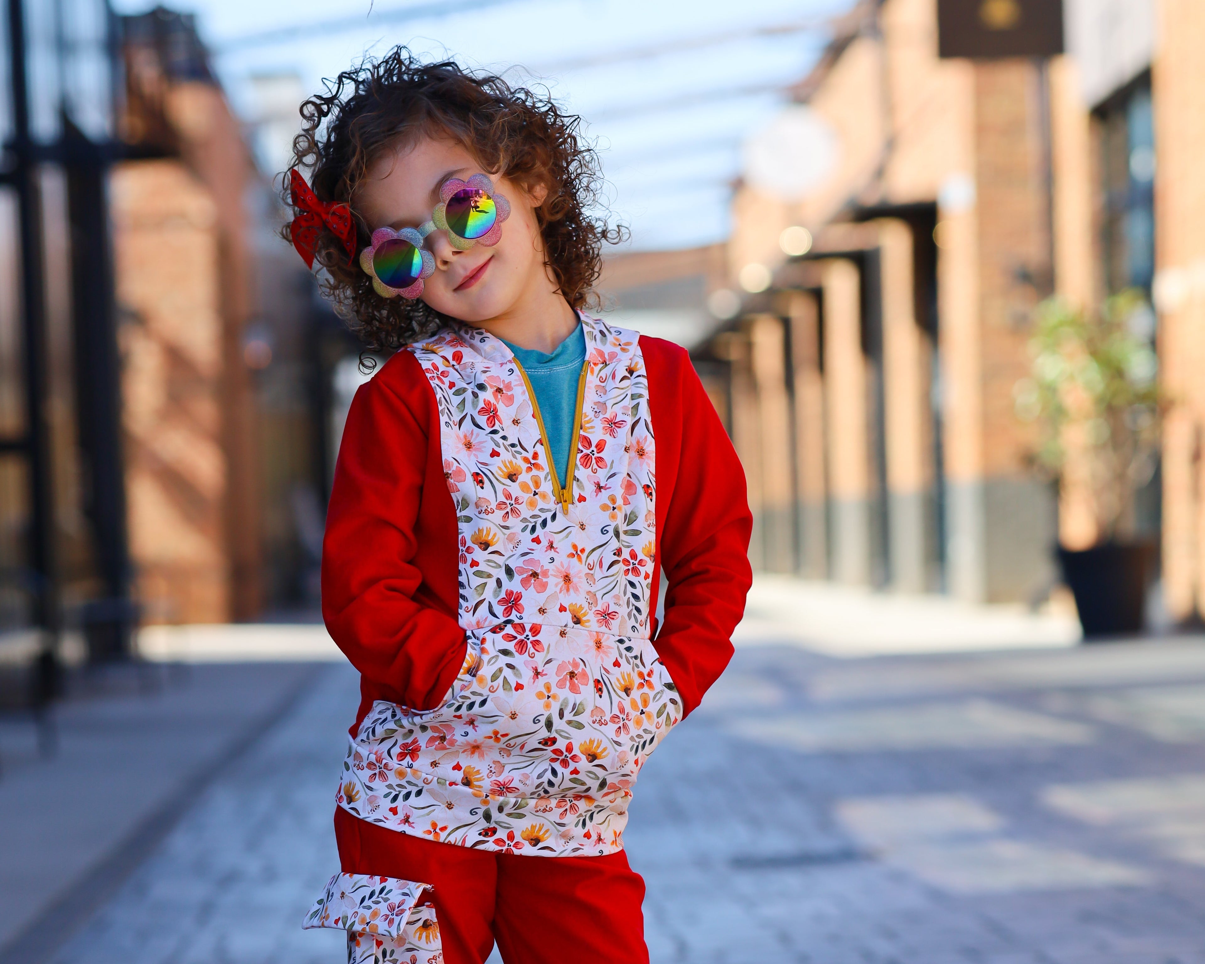 A child model wearing red cross cut cargos with a floral pattern on the pockets, paired with a white top and multicolored sneakers.